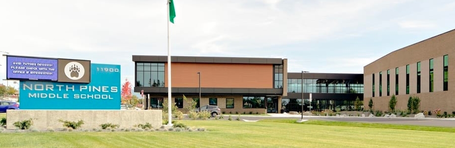 an image of north pines middle school with a sign, flag pole, and building with grass in the foreground